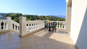 A balcony with a white balustrade, a table with chairs, and a view of green hills and mountains in the distance. - -Bright villa, pool, air conditioning, near St-Florent- sleeps 6 (Oletta)