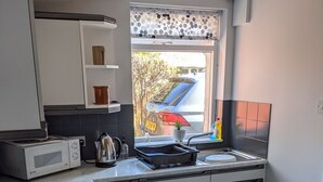 Eine moderne Küche mit weißen Schränken, einer eingebauten Mikrowelle, einem Wasserkocher und einem Fenster mit Blick auf einen parkenden Wagen vor dem Haus.