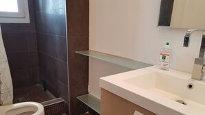 Kylpyhuone, jossa on wc, lasihylly, pesuallas ja pullo käsidesiainetta.
