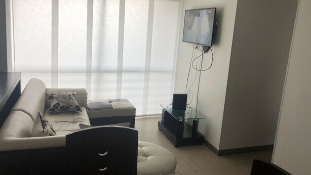 A modern living room with a sofa, ottoman, and a flat-screen TV mounted on the wall. - Tourist apart (Pereira)
