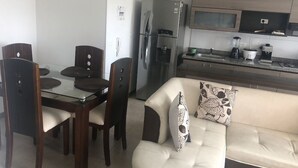 A modern kitchen with a refrigerator, microwave, and coffee maker. There is a dining table with chairs and a sofa with decorative pillows. - Tourist apart (Pereira)