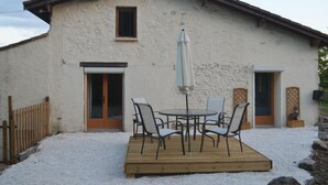 A rustic building with a wooden deck, outdoor seating, and a white exterior.