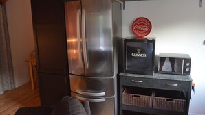A compact kitchen with a stainless steel refrigerator, a microwave, and a shelf with various containers.