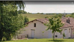 A rural house with a small porch, surrounded by greenery and a clear sky.