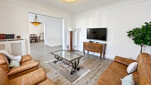 Ein geräumiges Wohnzimmer mit einer Ledersofa, einem Glastisch und einem Fernseher auf einem Holzboden.