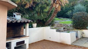Ein Patio mit Kamin aus Backstein, umgeben von üppiger Vegetation, darunter Palmen und weitere Pflanzen.