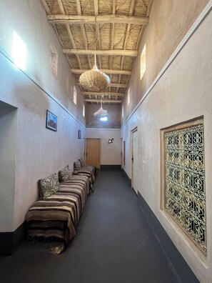 Un couloir où s’alignent plusieurs lits le long d’un mur, un luminaire suspendu et, sur le mur opposé, une grille décorative en métal.