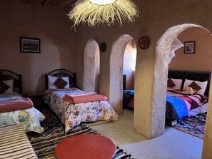 Een klassieke kamer met twee bedden, een geweven plafondlamp en uitzicht door een boog.