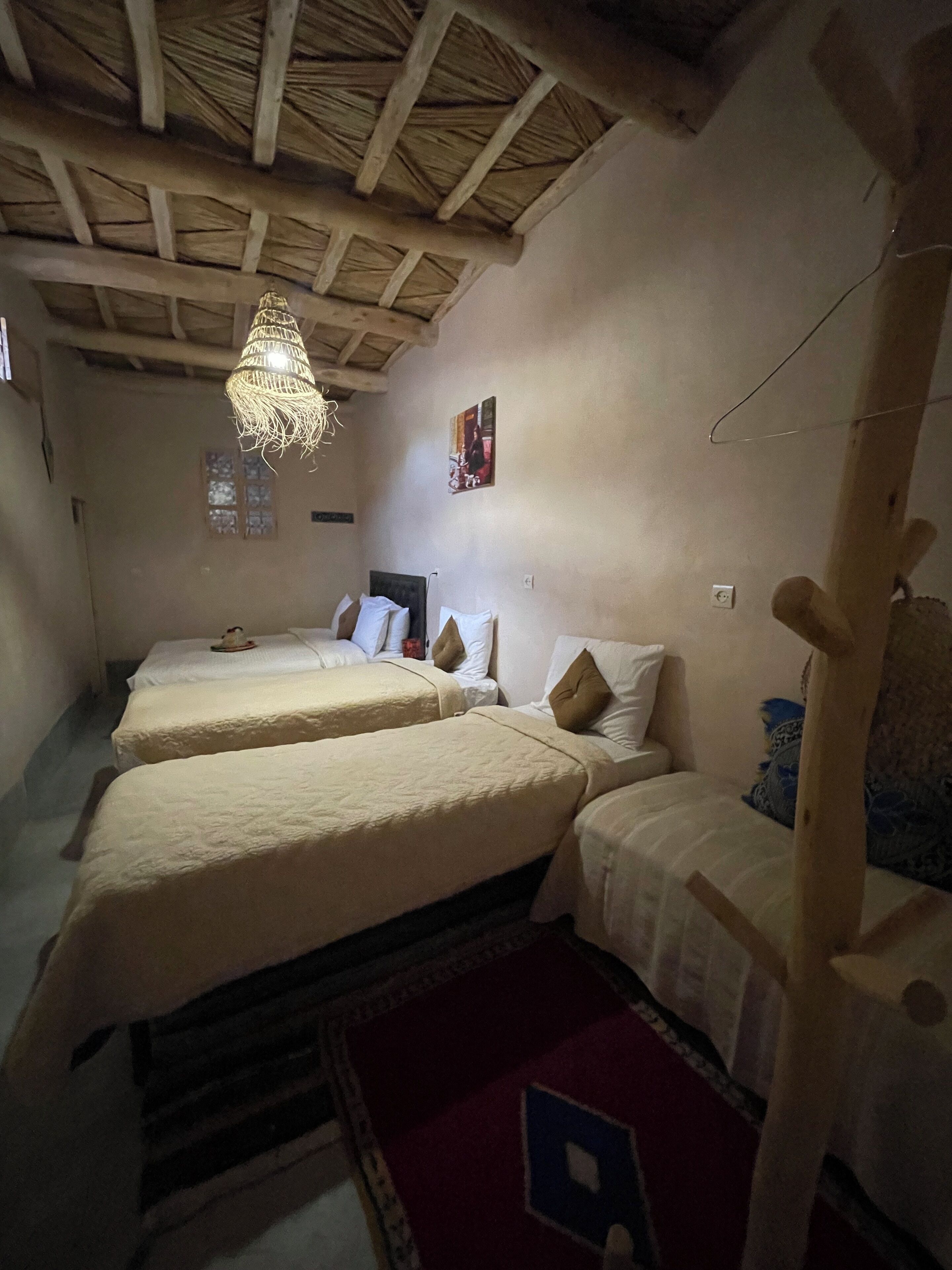 Een kamer met drie bedden, een houten plafond, een hanglamp en een aan de muur bevestigd schilderij.