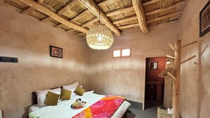 A bedroom with a bed, a hanging light fixture, a wooden coat rack, and a small chair.