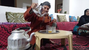 Une personne verse du thé d’une théière en argent dans des verres posés sur un plateau.