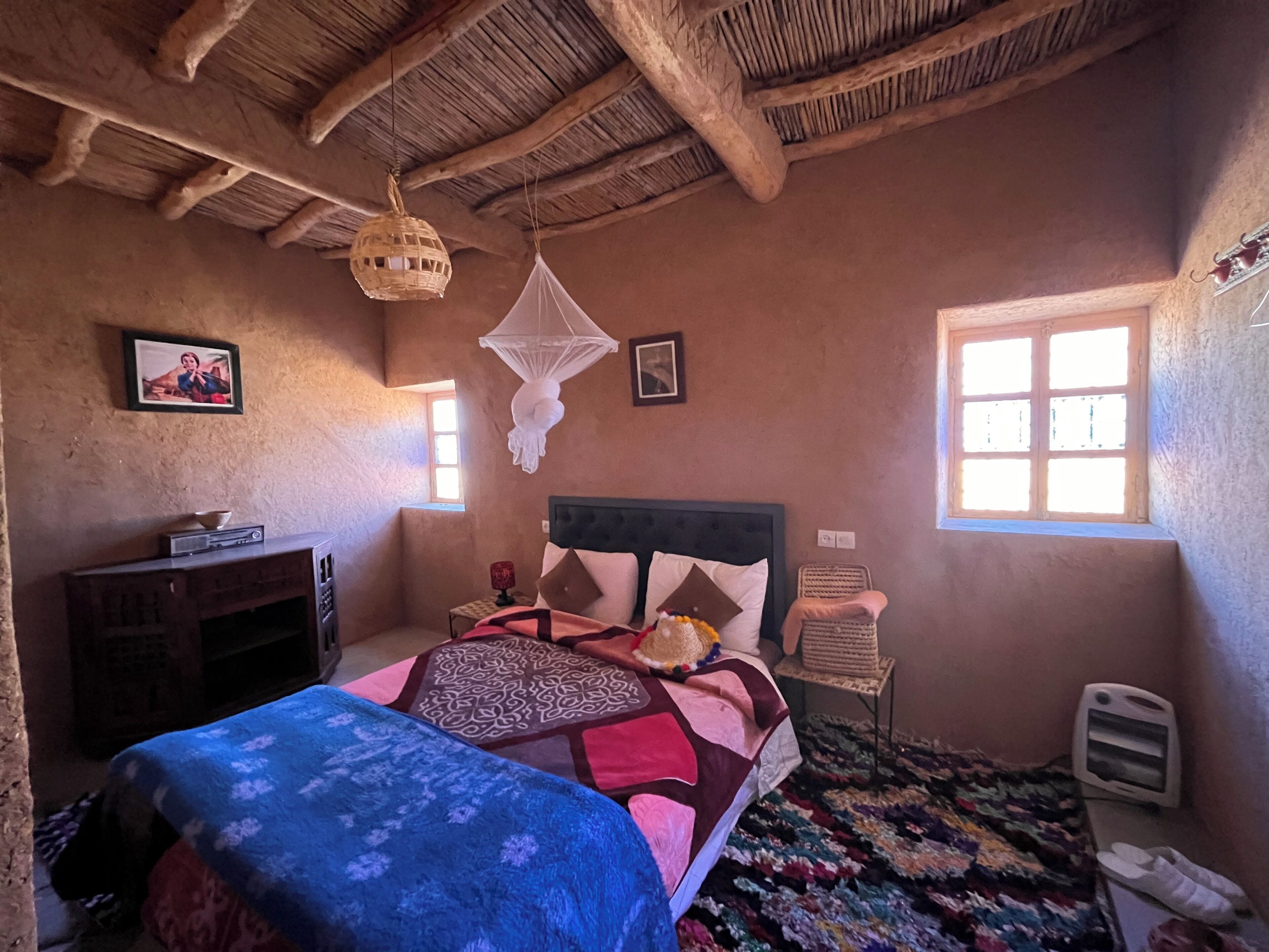Un dormitorio con cama, mesita de noche, silla, ventana y ventilador de techo.