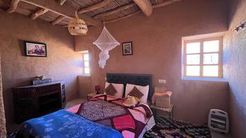 Un dormitorio con cama, mesita de noche, silla, ventana y ventilador de techo.