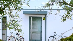 A modern building with a white exterior and a grey door. There are two bicycles parked outside, and the ground is covered with gravel. - MONTE DA FIFAS Countryside house with a pool and a magnificent view over the dam (Montargil)