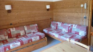 Une cabane en bois avec deux bancs en bois dotés de coussins à motifs, une petite table en bois et un téléphone fixé au mur.