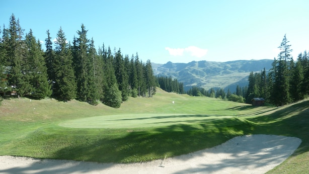 Un parcours de golf avec un bunker de sable, des arbres et des montagnes à l’horizon.