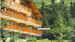 Un immeuble à plusieurs étages doté de balcons, entouré d’une végétation luxuriante et de montagnes.