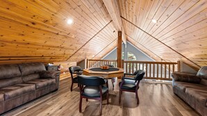 Ein gemütliches Schlafzimmer im Loft-Stil mit Holzboden, Holzbalkendecke, einem runden Tisch mit Stühlen und einem braunen Ledersofa.