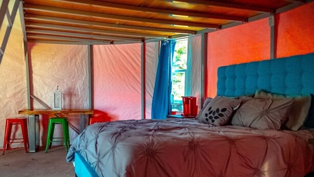 Un dormitorio con una cama, un escritorio y taburetes de colores.