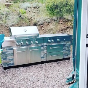 An outdoor kitchen with a grill, two ovens, and a sink.