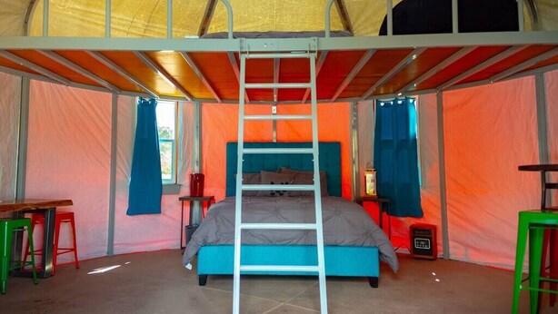 Una tienda de campaña con una cama litera, una escalera y una pequeña mesa con una silla.