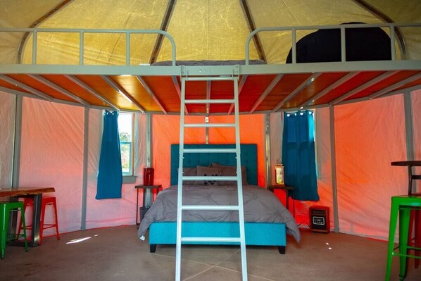 A tent with a bunk bed, a ladder, and a small table with a chair.