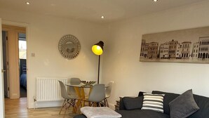 A modern living room with a grey sofa, a wooden coffee table, and a dining area with a table and chairs.