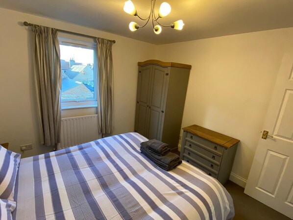 A bedroom with a bed, a dresser, a wardrobe, a window with curtains, and a chandelier. - Penthouse Waterfront Apartment - St Neots (Saint Neots)