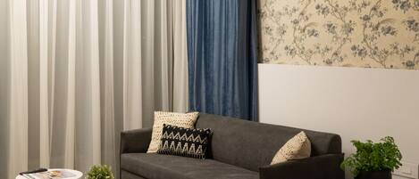 A modern living room with a grey sofa, a round coffee table, and a blue bed.