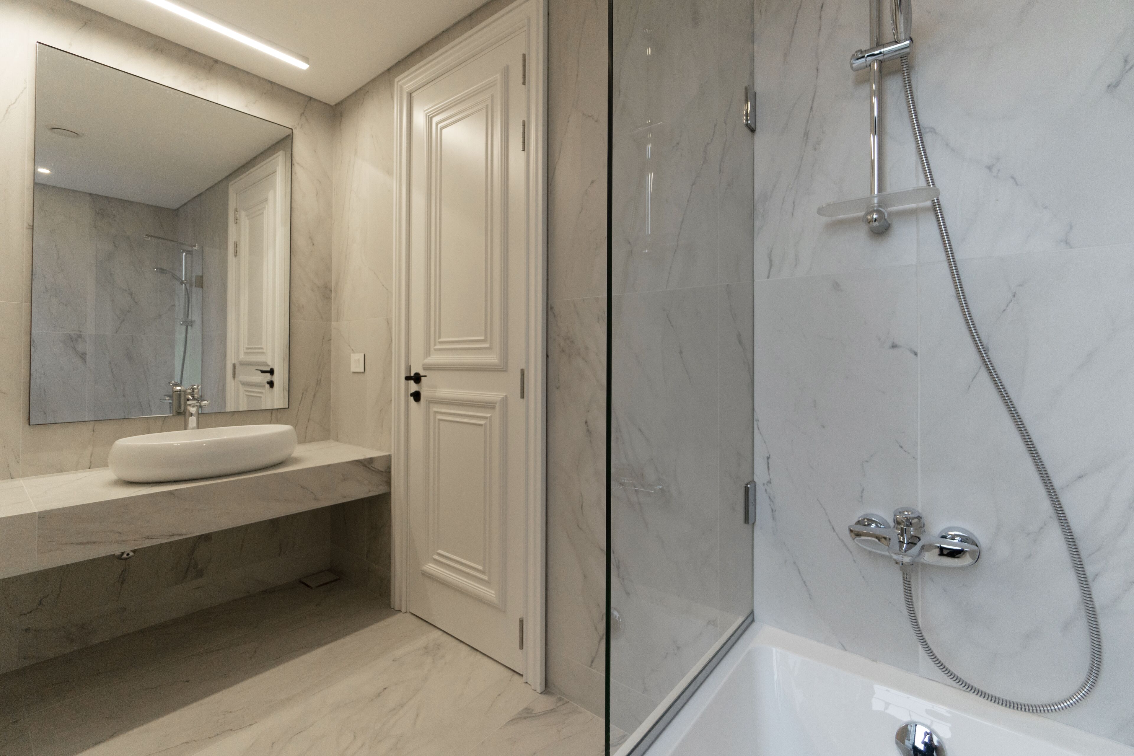 Un bagno moderno con lavabo in marmo, uno specchio grande e cabina doccia in vetro.