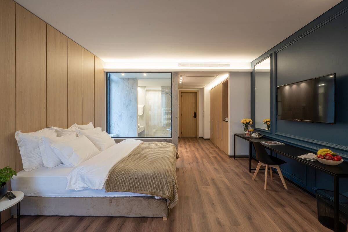 A modern hotel room with a large bed, a desk, a flat-screen TV, and a view of the bathroom.