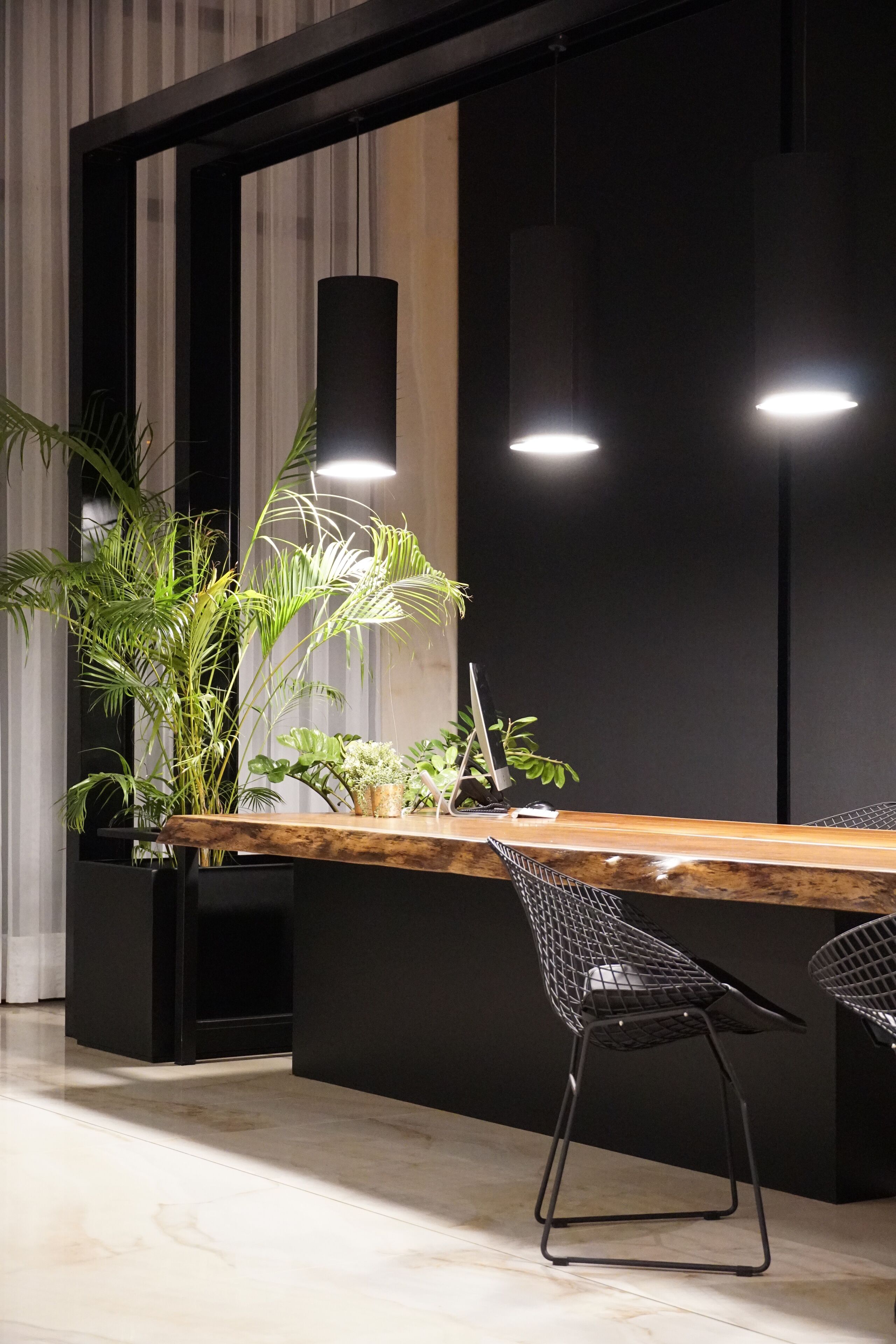 Een moderne receptiebalie met een houten toonbank, zwarte metalen stoelen en potplanten.