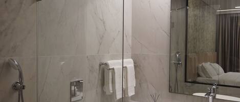 A modern bathroom with a glass-enclosed shower, a white toilet, a large mirror, and a sink with a round basin.
