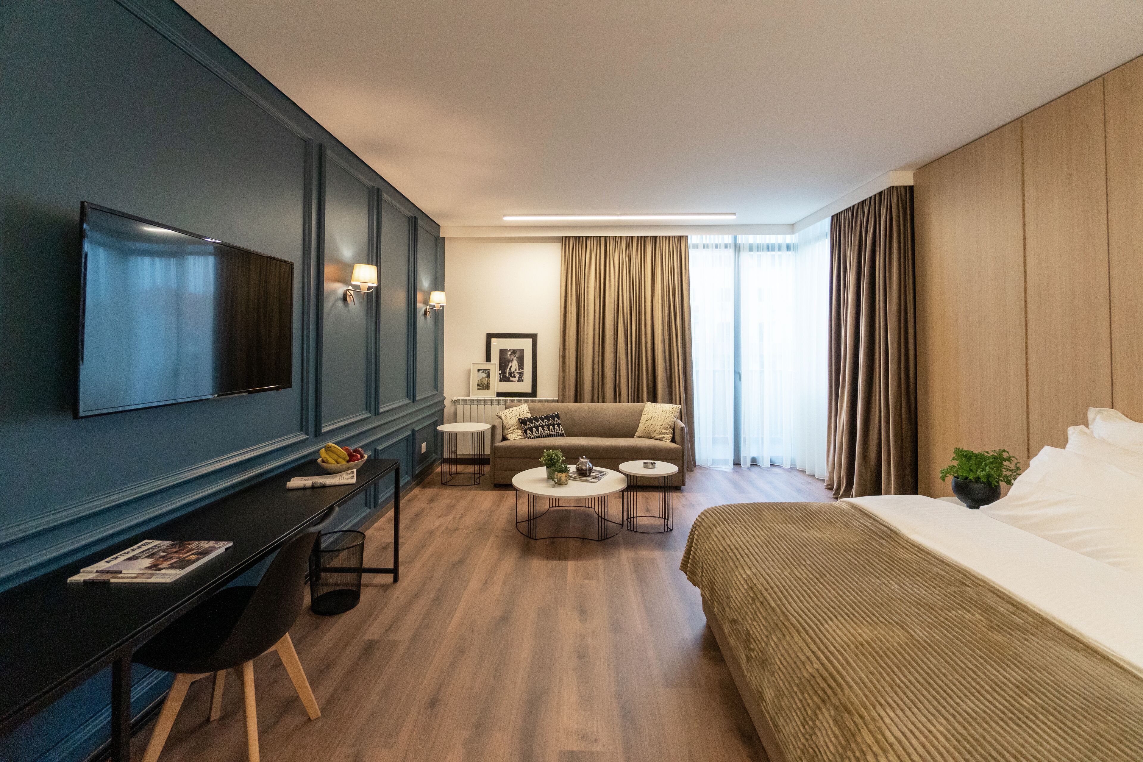 Una habitación de hotel moderna con televisión de pantalla plana, un sofá, una cama, un escritorio con una silla y una mesita de centro.
