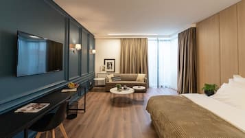 A modern hotel room with a flat-screen TV, a sofa, a bed, a desk with a chair, and a small coffee table.