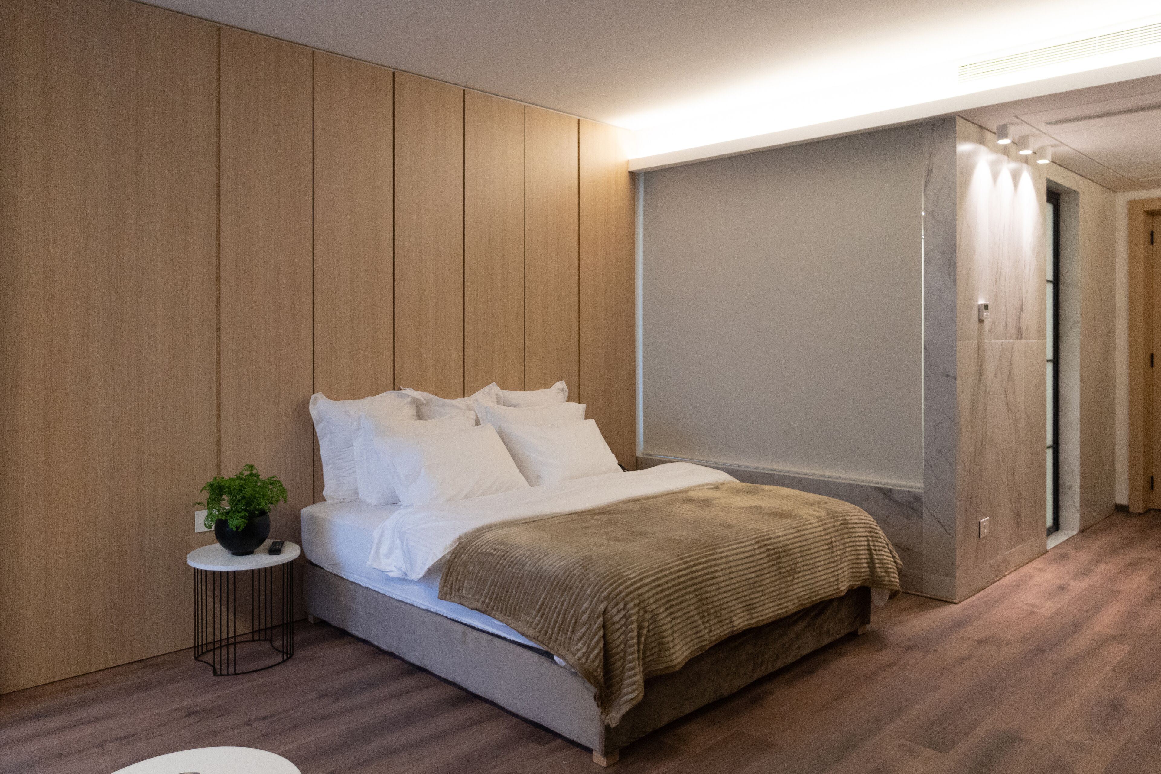 A modern bedroom with a bed, a side table with a plant, and a wardrobe.