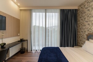 Una habitación de hotel con una cama, un escritorio, una silla, un cesto de basura y una ventana con cortinas.