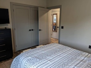 A bedroom with a bed, a dresser, and a TV. There are two doors and a hallway leading to another room.