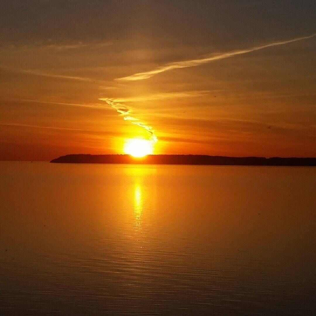 A sunset over a calm body of water with a silhouette of land in the distance.