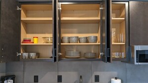 A kitchen with open cabinets, a coffee maker, a sink, and a microwave. - Modern Luxe Condo | Walk to Downtown TC | State 210 (Traverse City)