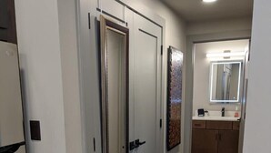 A hallway with a wooden floor, a mirror above the sink, and a door with a handle. - Modern Luxe Condo | Walk to Downtown TC | State 210 (Traverse City)