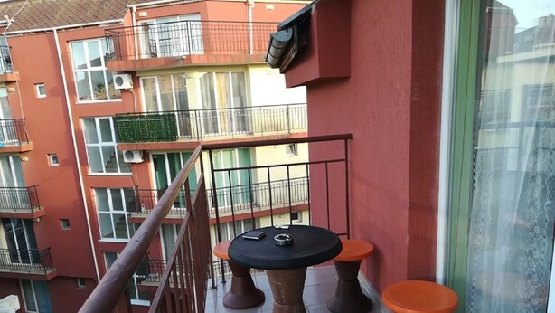 Ein Balkon mit einem runden Tisch, vier orangefarbenen Hocker, einem Metallgeländer und Blick auf angrenzende Gebäude.
