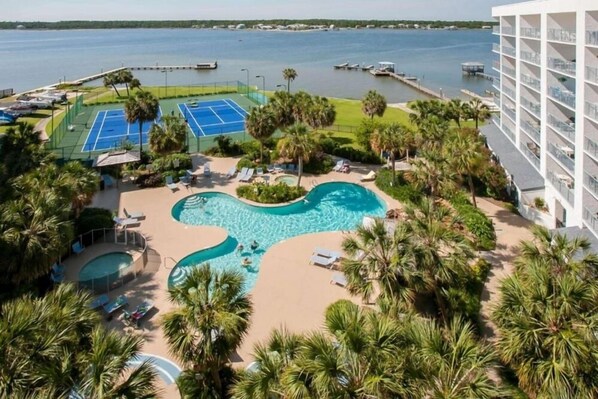 A hotel with a large swimming pool, tennis courts, and a view of the water.