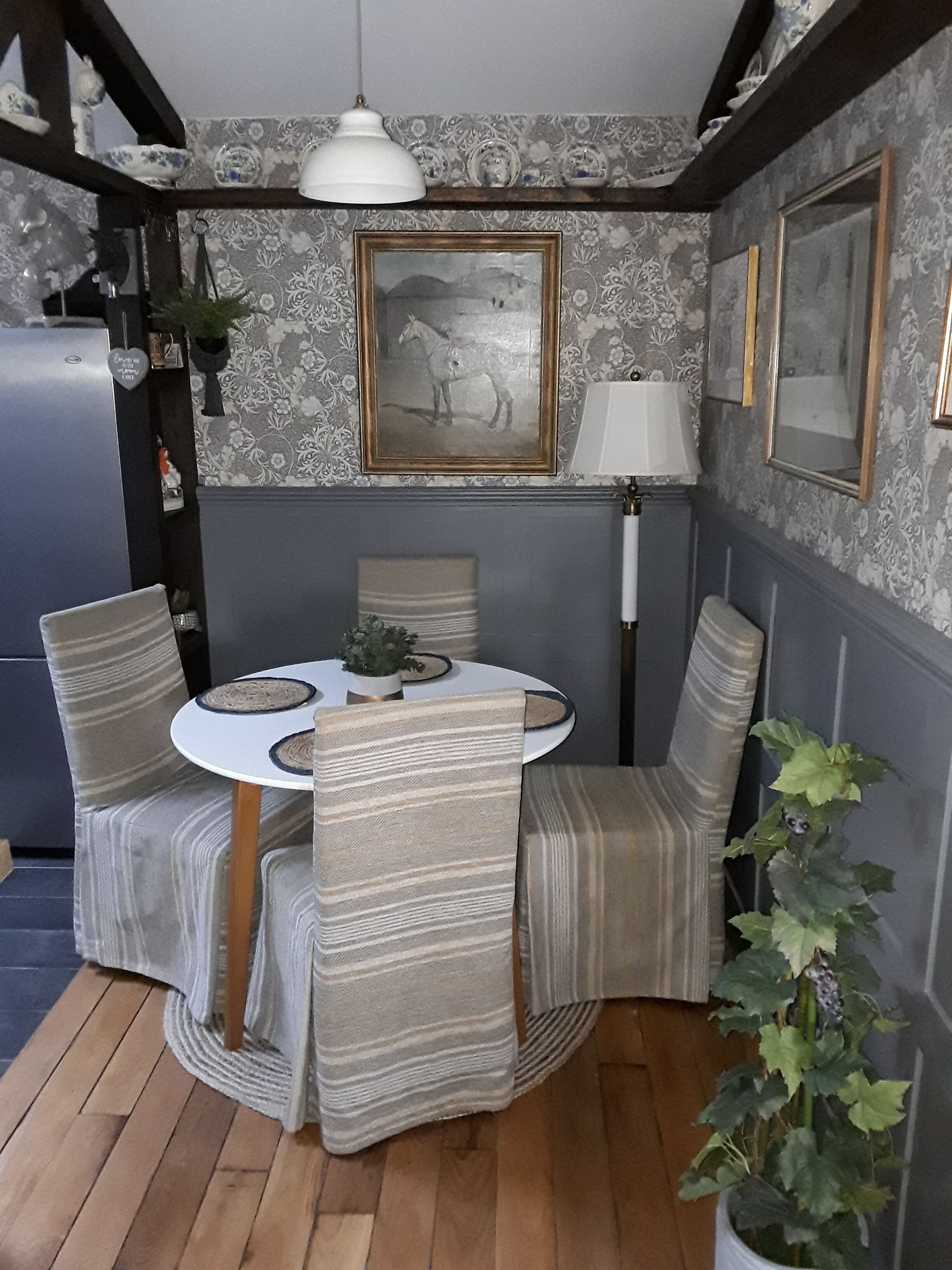 Un comedor con una mesa redonda, sillas a rayas, una lámpara blanca y un cuadro en la pared.