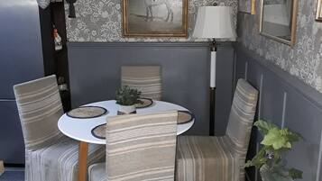 Un comedor con una mesa redonda, sillas a rayas, una lámpara blanca y un cuadro en la pared.