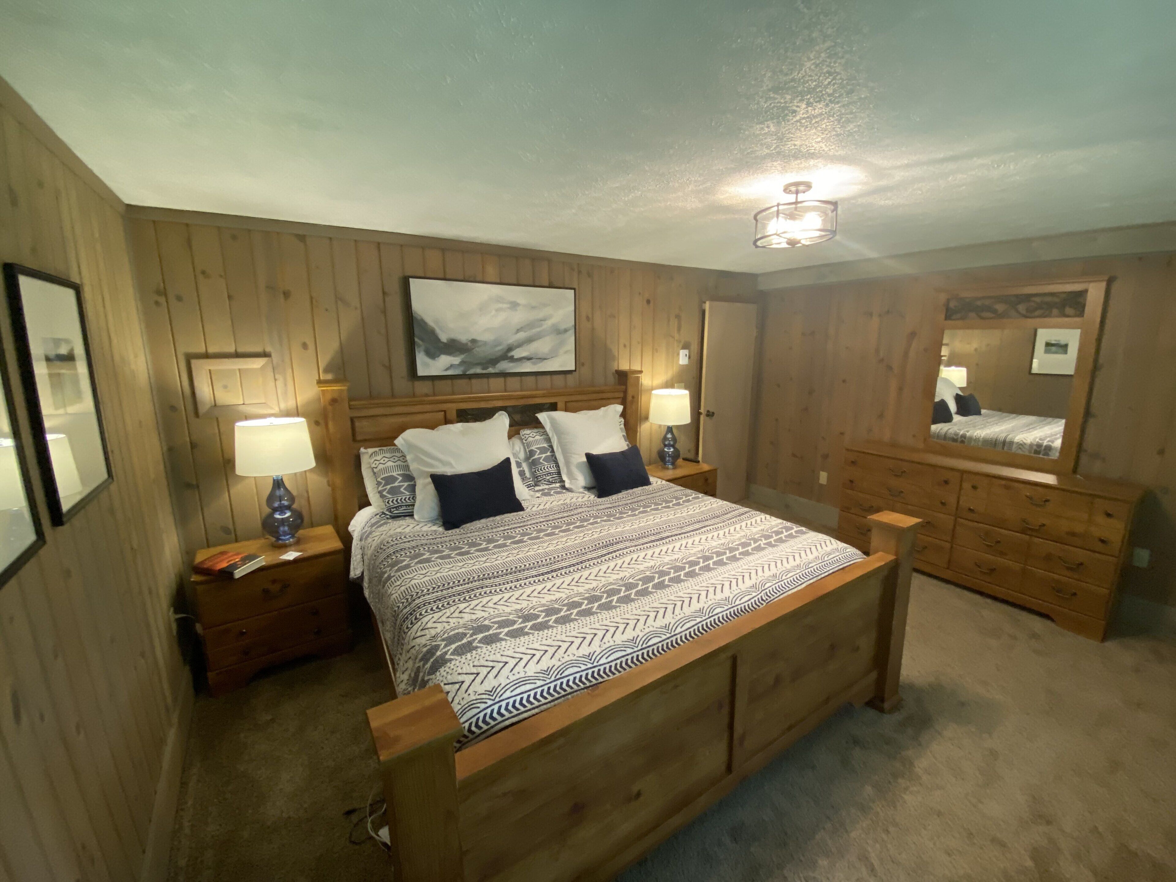 A wooden-paneled bedroom with a bed, nightstands, a dresser, and a mirror.