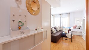 Ein modernes Wohnzimmer mit einer Couch, einem Couchtisch und einem kleinen Beistelltisch. An der Wand hängt ein Spiegel und eine Holzregal zeigt dekorative Gegenstände.