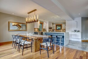 Een moderne keuken met een centraal eiland, een bar met zitplaatsen, en een eetgedeelte met een houten tafel en stoelen.