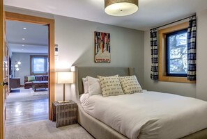 Een slaapkamer met een groot bed, een raam met ruitgordijnen, een aan de muur hangend kunstwerk en een radiator.