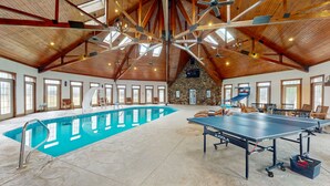 Indendørs swimmingpool med et bordtennisbord, træbjælker og stenvægge.